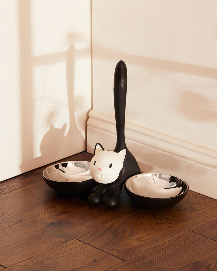 The Tigrito dual cat bowl for food and water features a cartoon black and white cat flanked by two bowls blending black thermoplatic on the outside and stainless steel inner for hygiene. Ideal alternative to boring food bowls for cat owners
